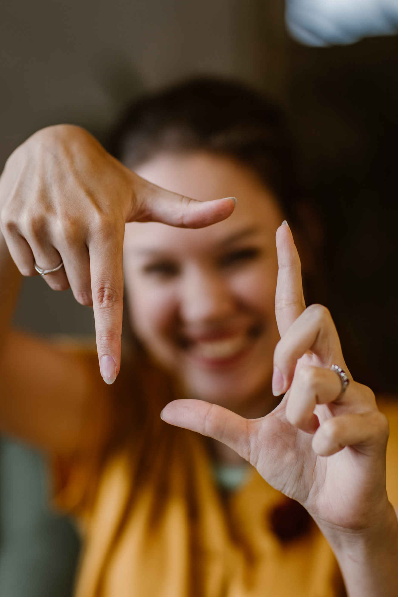 Foto door Marijn de Wijs: Op de foto lach ik wazig op de achtergrond naar de camera, voor in beeld zijn scherp mijn handen waarmee ik met duimen en wijsvingers een rechthoek uitbeeld.