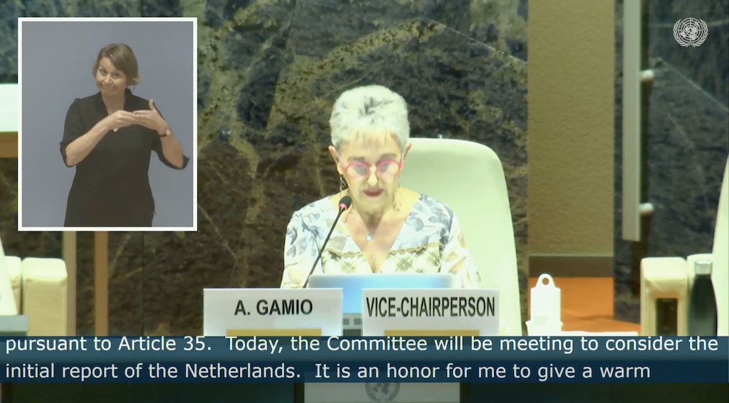 Schermafbeelding van de hoorzitting. Vice-voorzitter mevr. Gamio is in beeld, zij is een witte vrouw met kort grijs haar. Links in beeld is de gebarentolk. Onder in beeld is in Engelse ondertiteling te zien dat de zitting vandaag over Nederland gaat.