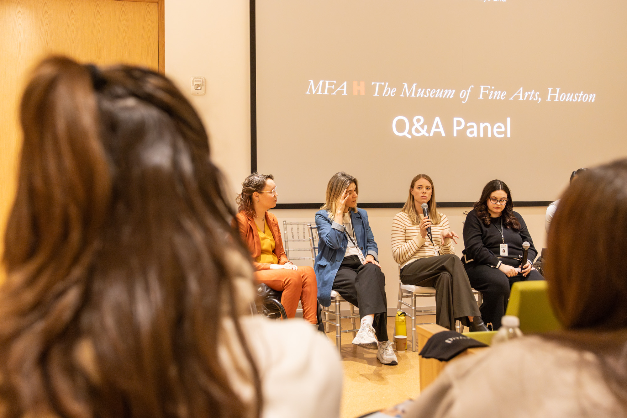 Foto door Jens Van Hecke: op de voorgrond vaag twee achterhoofden, daar tussendoor is een deel van het panel te zien bij het symposium. Op de achtergrond een donker scherm met daarop het logo van het Museum of Fine Arts Houston en de tekst "Q&A Panel".