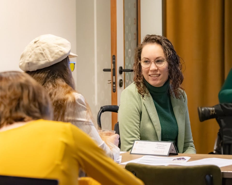 Jiska is te zien in gesprek met deelnemers. Zij is een indo vrouw met donker golvend haar en zit in een rolstoel. 