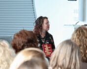 Foto door Jens Van Hecke: ik zit vooraan een zaal met het boek "Een staat van vrijblijvendheid" op mijn schoot en kijk naar rechts. Op de voorgrond vage achterhoofden van het publiek. Ik ben een indo vrouw met donker golvend haar, draag een dun bruin montuur bril en een donkere jurk met lange mouwen.